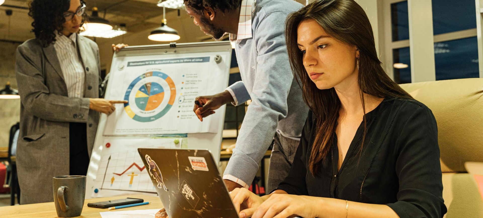 Professional team collaborating in a modern office, analyzing business charts and data on a flipchart and laptop.